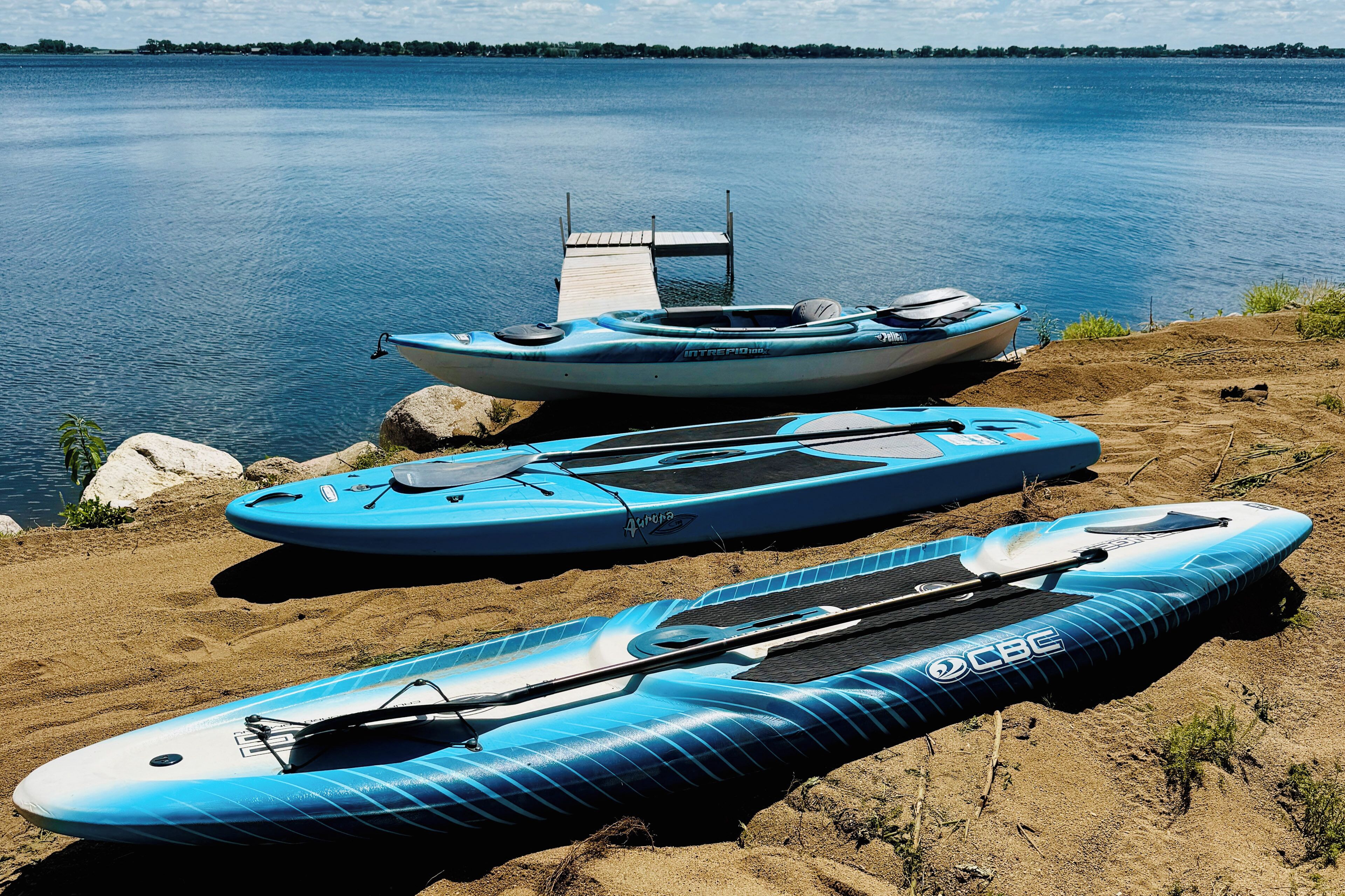 A dock with kayaks and a paddleboard by a calm lake.