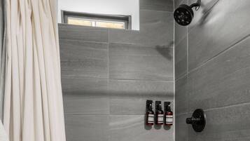 A modern bathroom with grey tiles, a showerhead, and three bottles of toiletries.