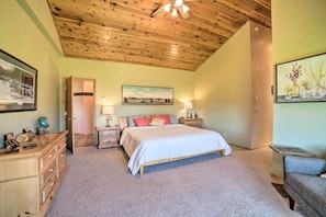 Quarto com teto de madeira, cama com roupa de cama branca, duas mesas de cabeceira com abajures, cômoda e um quadro na parede.