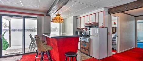 Une cuisine moderne avec un îlot central rouge, des tabourets de bar et une vue à travers la porte vitrée.