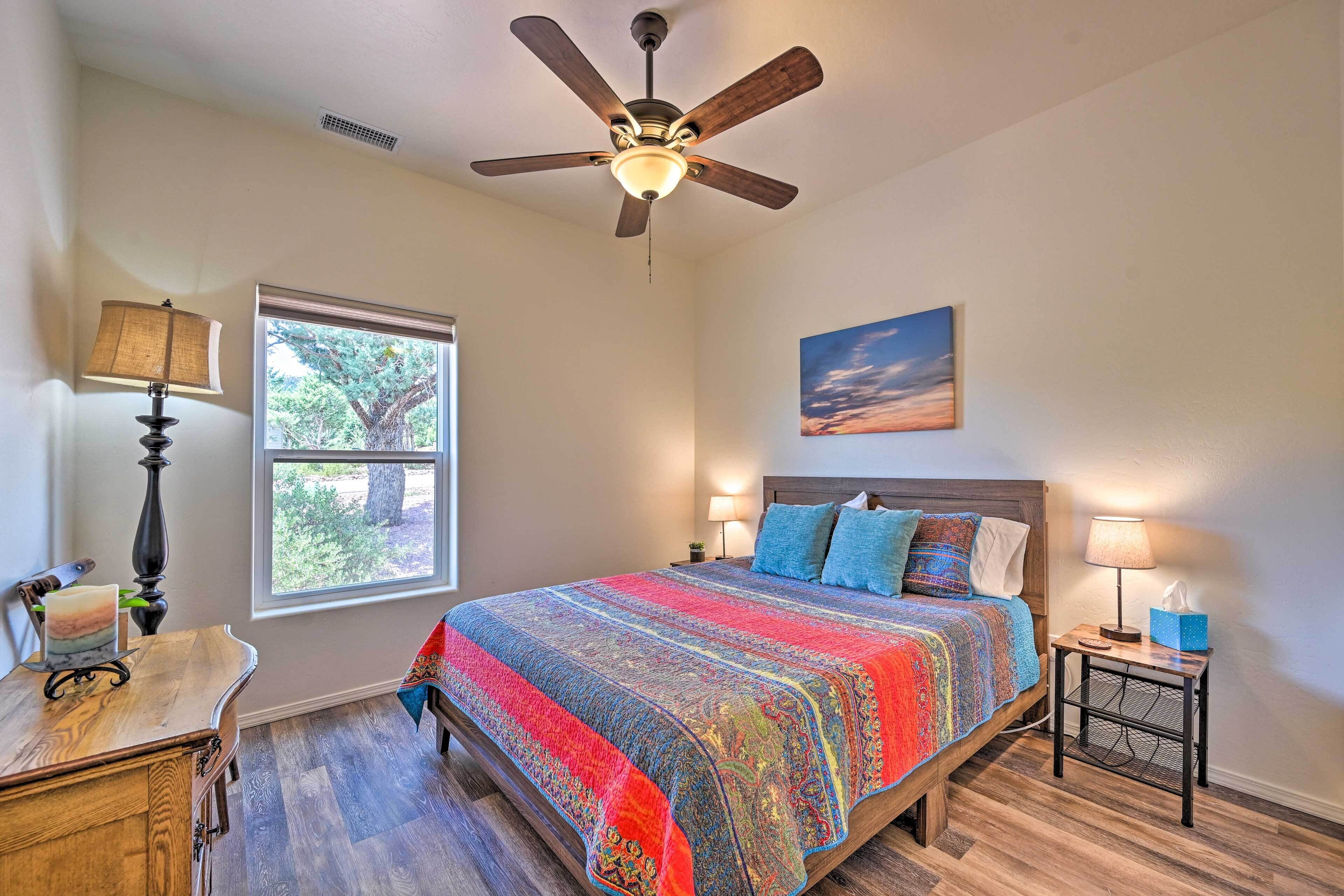 A bedroom with a bed, a ceiling fan, a window, a nightstand, and a lamp.