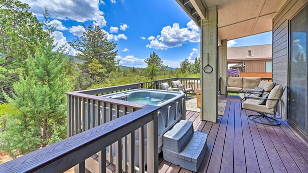 Een hottub op een houten terras met buitenmeubilair, omgeven door bomen en een heldere lucht.