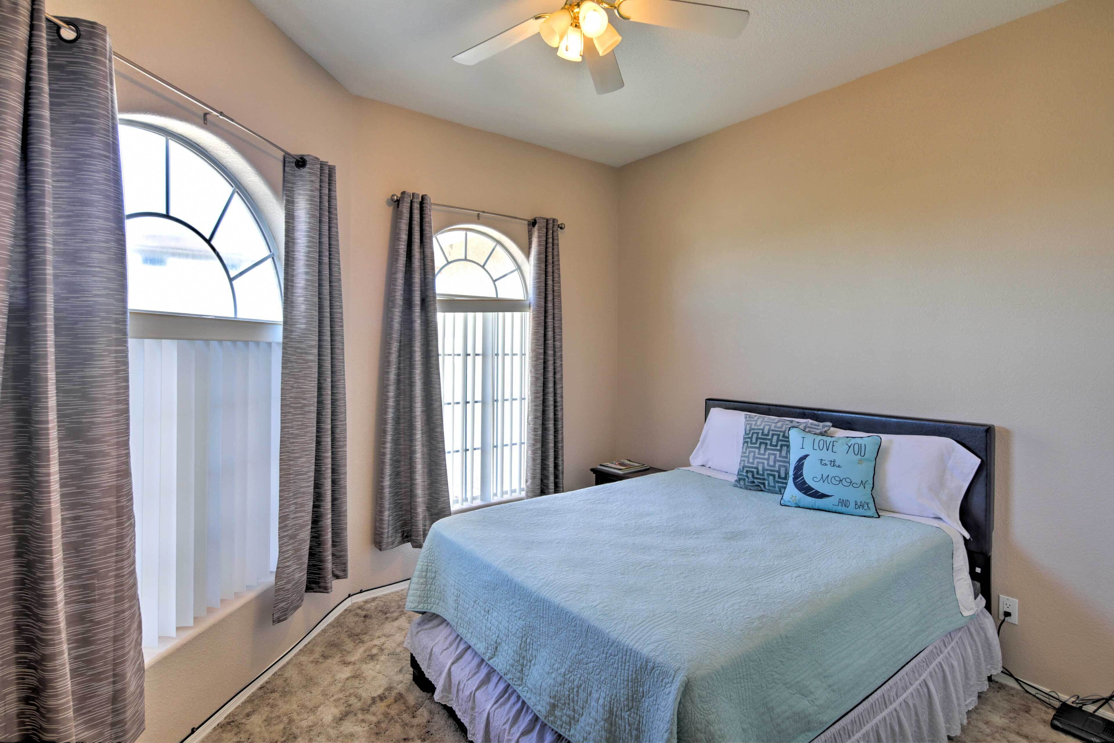 A bedroom with a bed, a ceiling fan, and a window with curtains.