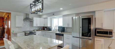 A modern kitchen with white cabinets, stainless steel appliances, a granite countertop, and a dining area with white chairs.