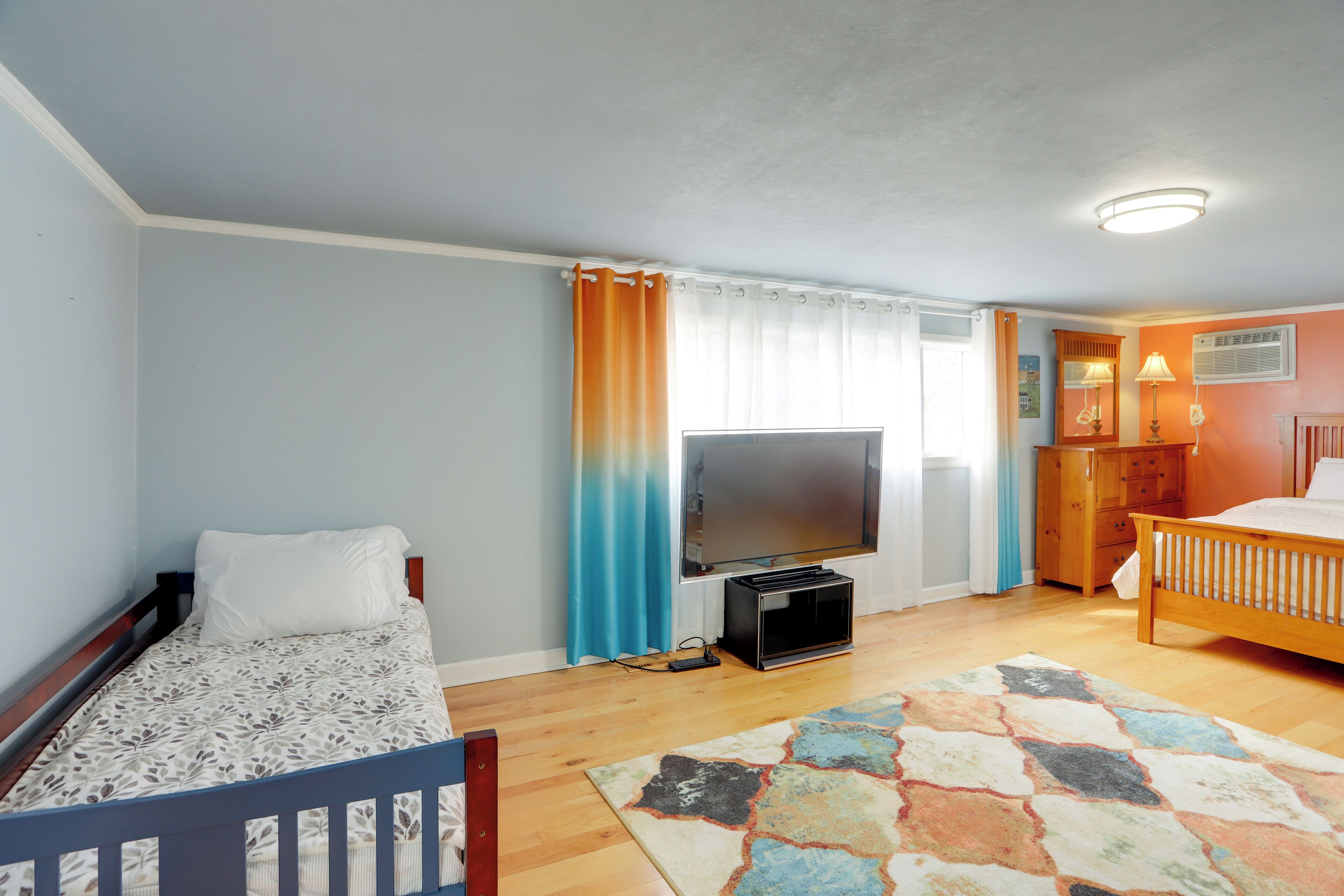 A bedroom with a bed, a TV, a dresser, and a window with curtains.