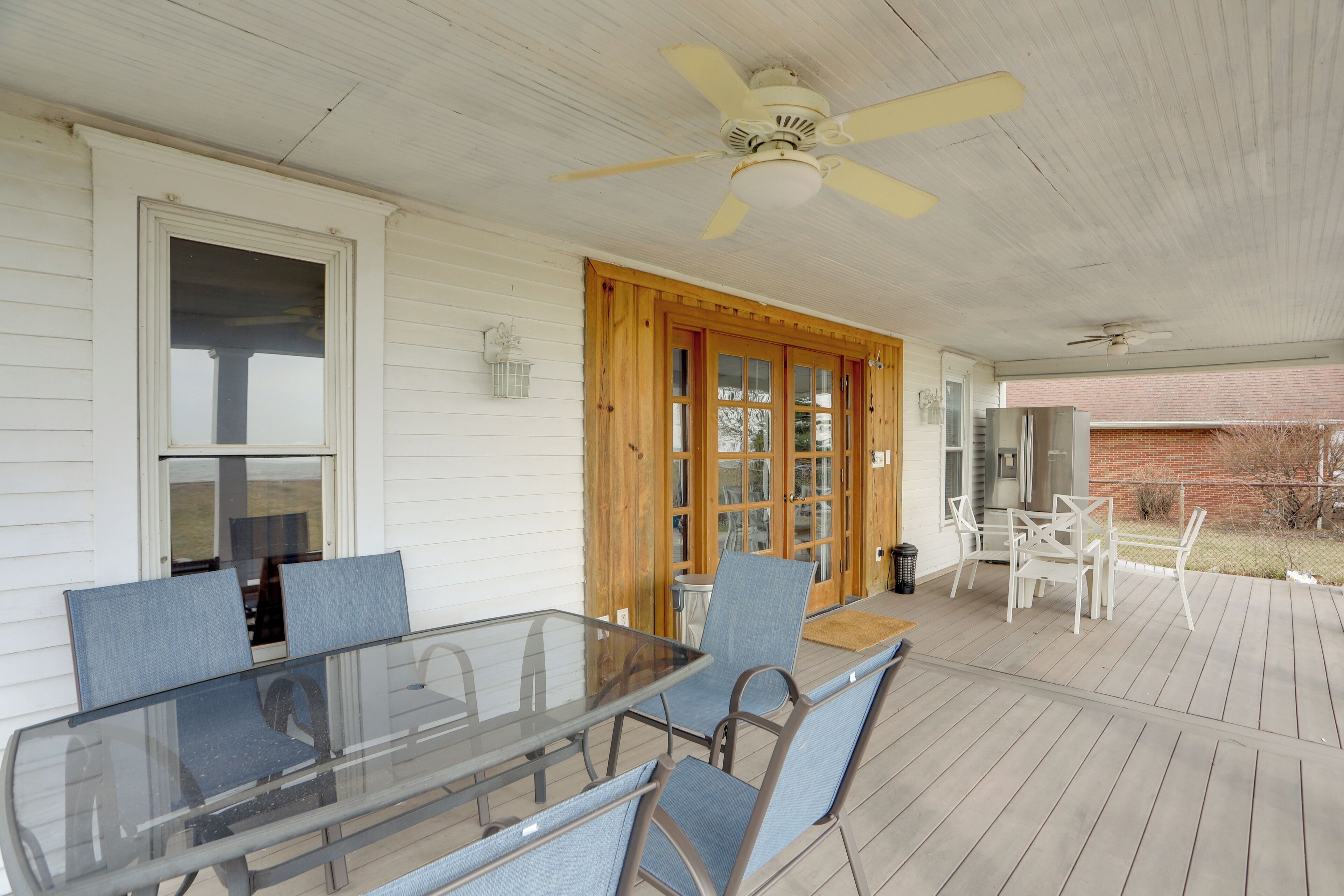 A covered patio with a glass table and chairs, wooden doors, and a ceiling fan.