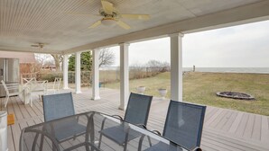 Een overdekt terras buiten met een glazen tafel en stoelen, witte zuilen en uitzicht op de oceaan.