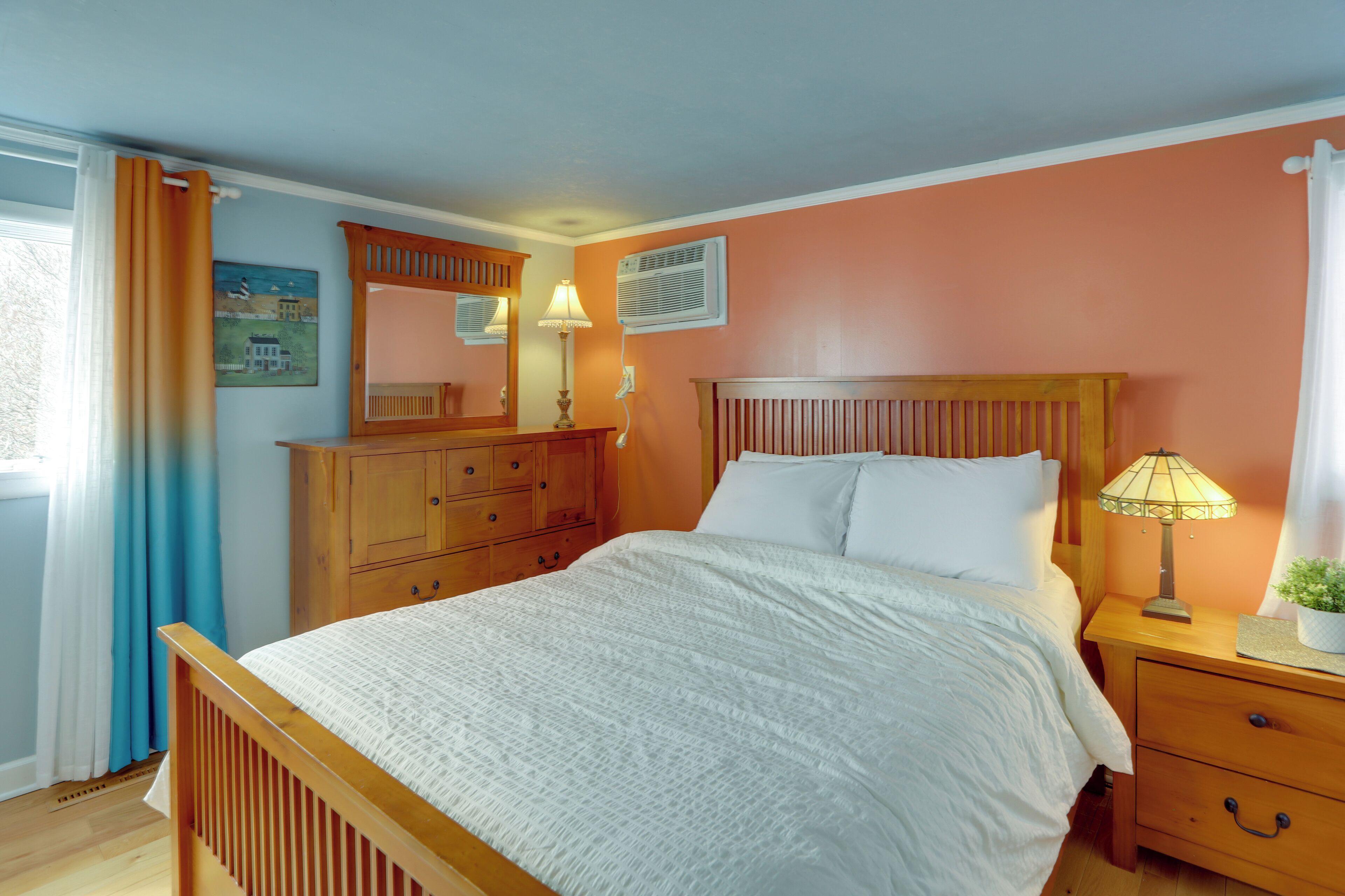 Une chambre à coucher avec un lit en bois, une table de chevet avec une lampe, une commode et une fenêtre avec des rideaux.