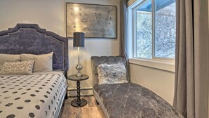 Un dormitorio con cama, una silla, una lámpara y una ventana con cortinas.