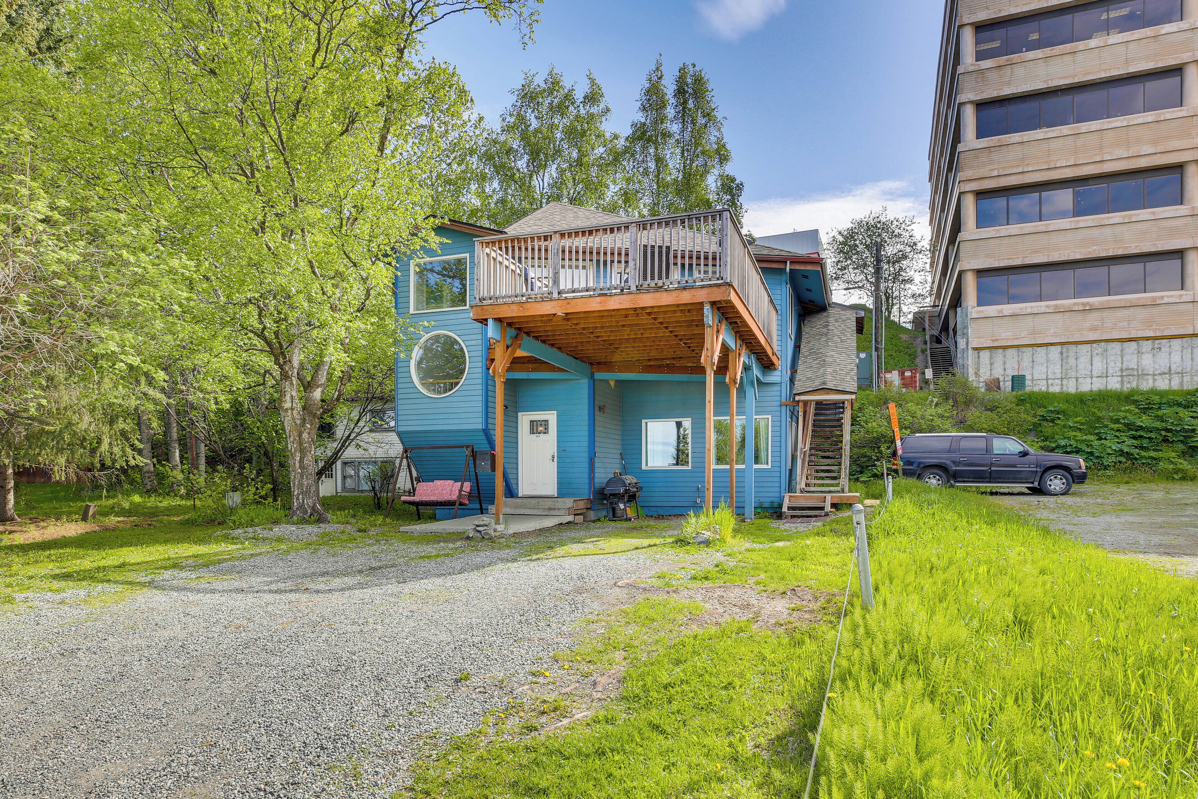 A two-story building with a balcony, a gravel driveway, and a car parked nearby.