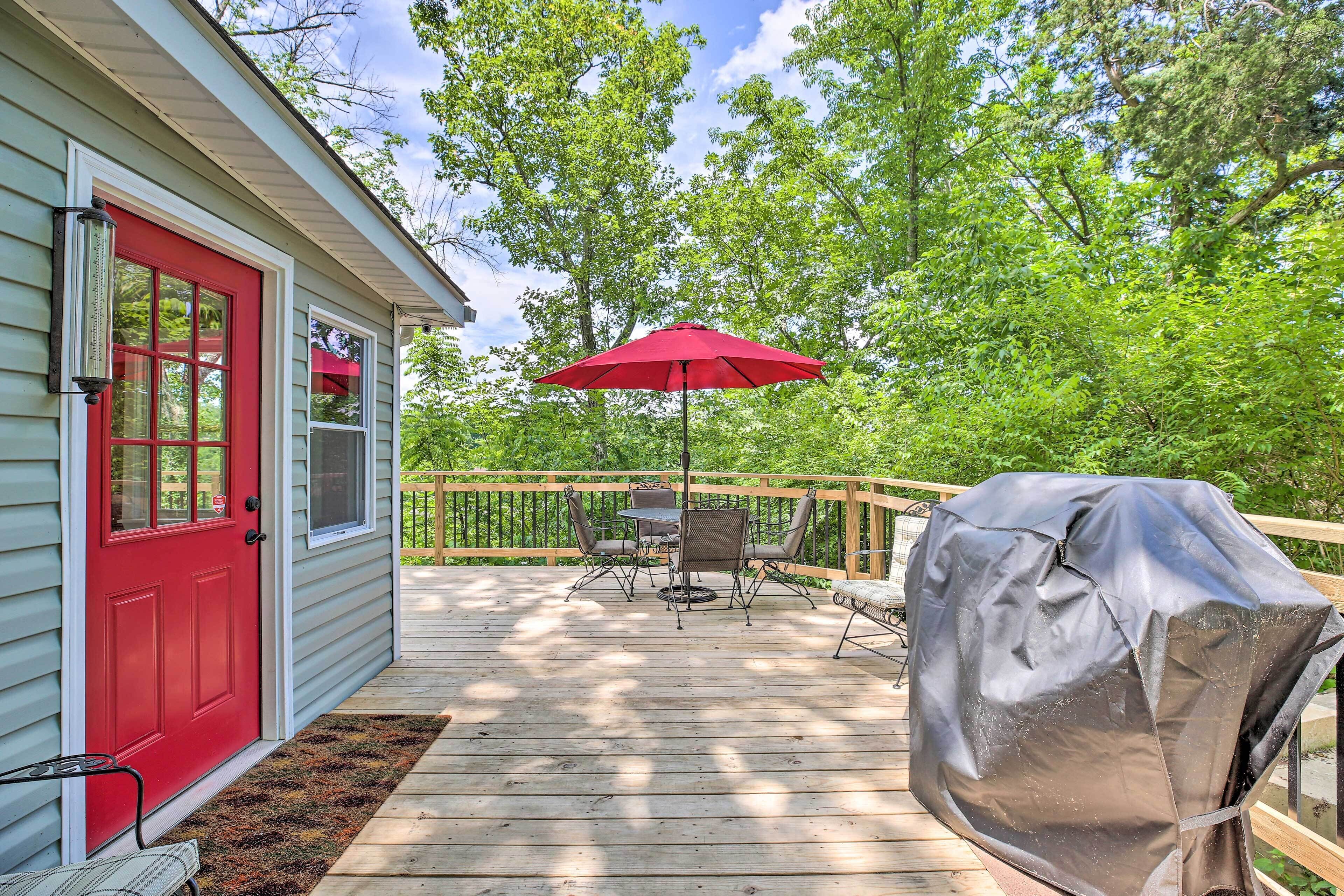 Une terrasse en bois avec une porte rouge, un barbecue abrité et du mobilier d’extérieur.