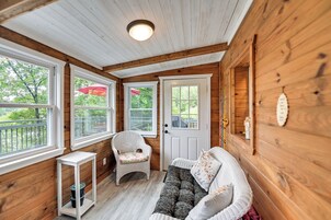 Interior de una cabaña de madera con un sofá blanco, un sillón de mimbre y una mesita.