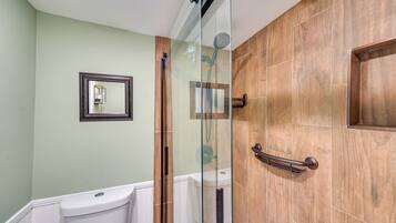 A bathroom with a glass-enclosed shower, a wooden door, a white toilet, and a framed mirror on the wall.