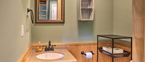 A bathroom with a wooden vanity, a sink, a mirror, a towel rack, and a metal shelf with toiletries.