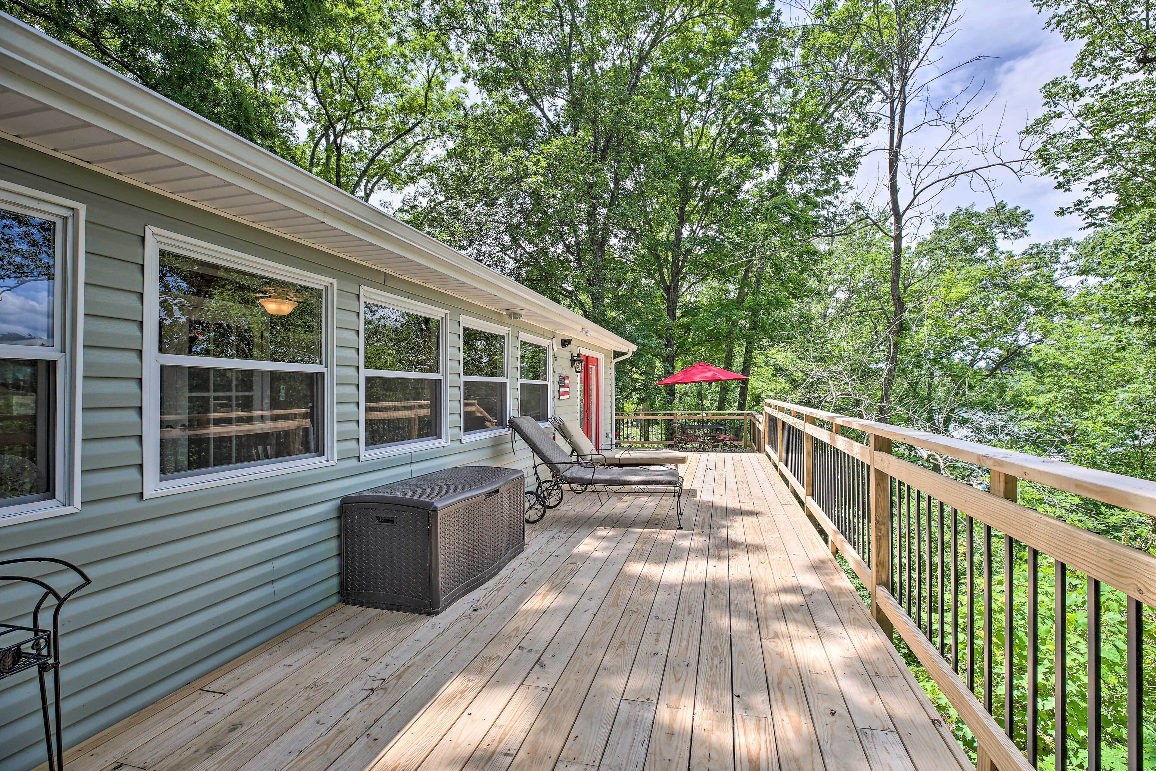 A wooden deck with two lounge chairs and a covered seating area, surrounded by trees.