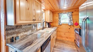A kitchen with wooden cabinets, a marble countertop, a stainless steel refrigerator, and a window with patterned curtains. - Our Lakeside Retreat w/ Deck on Lake Herrington! (Lancaster)