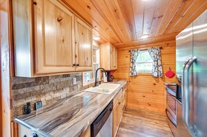Una cocina con armarios de madera, encimera de mármol, refrigerador de acero inoxidable y una ventana con cortinas estampadas.