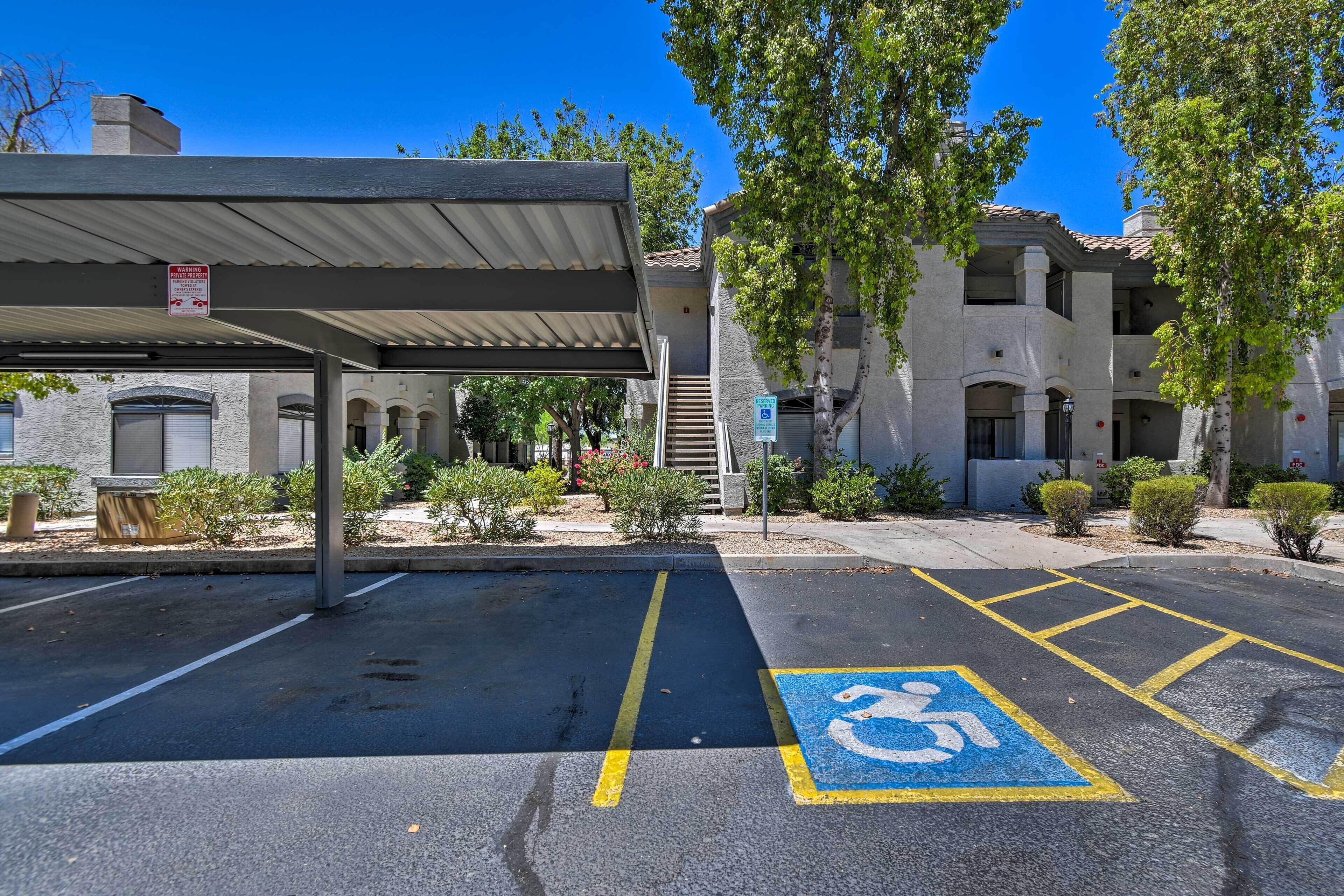 Un área de estacionamiento con espacios accesibles para personas con discapacidad, un paseo techado y un edificio de techo con tejas y ventanas arqueadas.