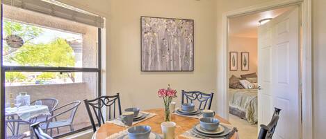 A dining area with a round table set for four, surrounded by chairs, and a window with blinds.