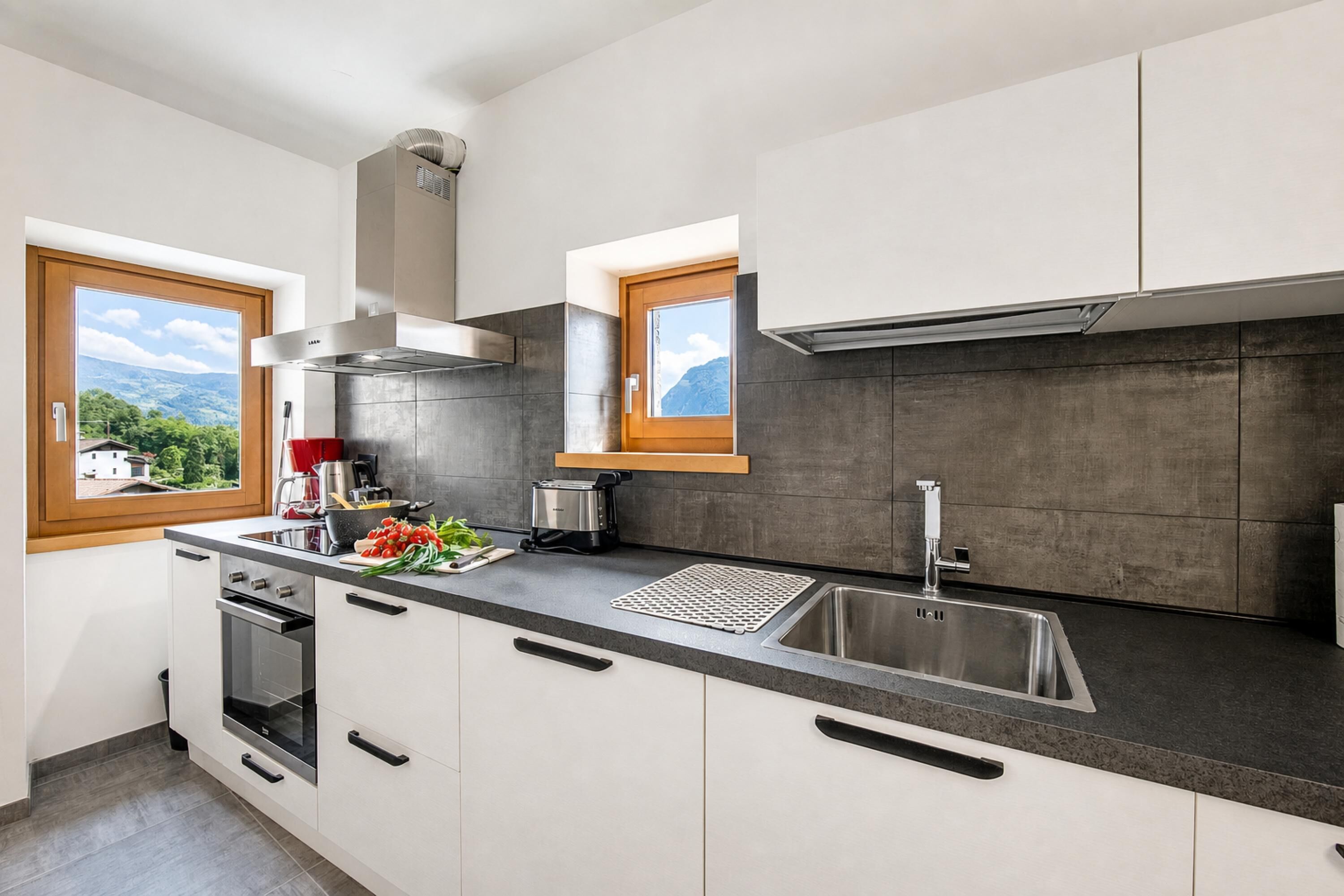 Une cuisine moderne dotée d’un grand îlot central, d’un four encastré et offrant une vue sur les montagnes par les fenêtres.
