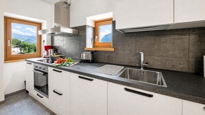 Une cuisine moderne dotée d’un grand îlot central, d’un four encastré et offrant une vue sur les montagnes par les fenêtres.