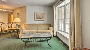 A living room with a green carpet, a sofa, a coffee table, a lamp, and a window with curtains. - Pigeon Retreat w/ Community Pool & Hot Tub! (Pigeon)