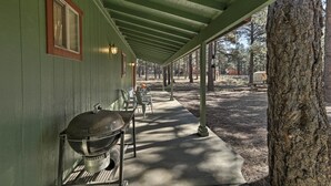 Un espace extérieur abrité, doté d’un barbecue et de chaises, et entouré d’arbres.