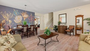 A spacious living room with a dining area, a staircase, and a large floral wall mural. - Greenview Bliss By Shine Villas #031 5 Bedroom Villa (Davenport)