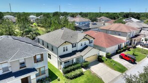 Zona residencial con casas de techos inclinados, paneles solares y un vehículo rojo estacionado en la calle.