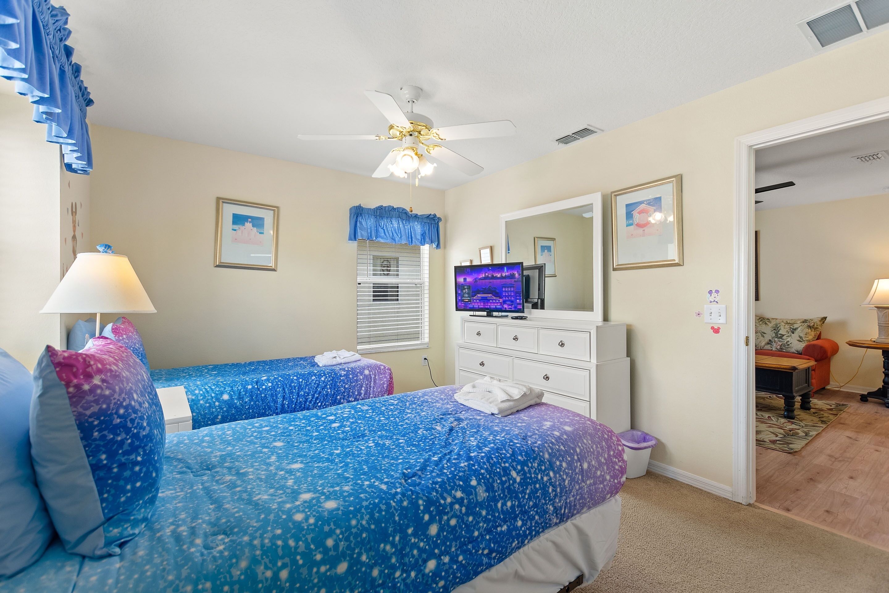 A bedroom with two beds, a ceiling fan, a TV, and a dresser.