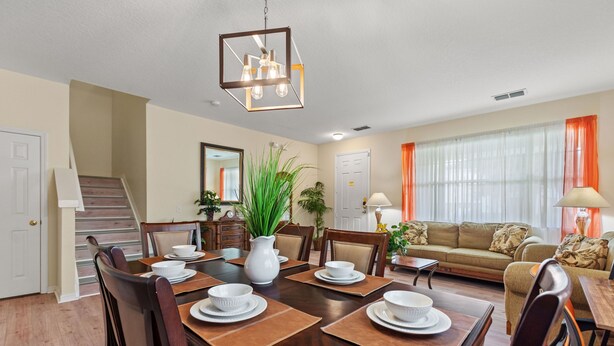 A dining area with a wooden table set for four, surrounded by chairs. A staircase is visible to the left, leading to another level. - Greenview Bliss By Shine Villas #031 5 Bedroom Villa (Davenport)