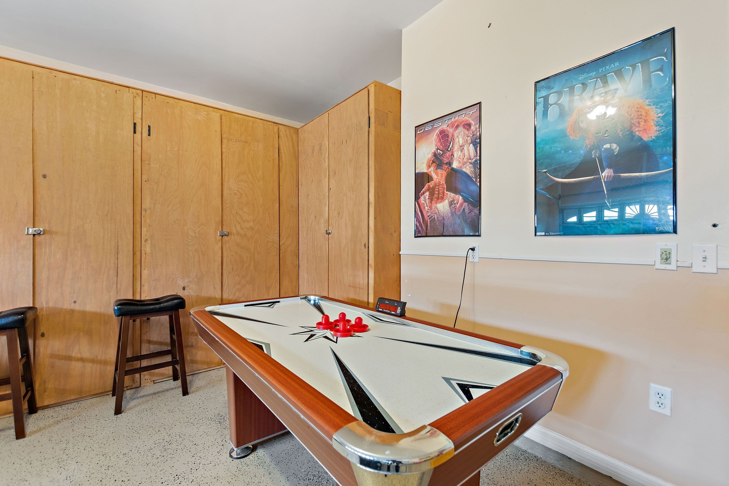 Une table de billard avec des tabourets, des meubles en bois et deux affiches encadrées au mur.