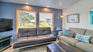 A living room with a dark leather sofa, a light-colored sofa with patterned cushions, a flat-screen TV, and a small side table. - Pet-friendly Ocean Park Home w/ Decks & View! (Ocean Park)