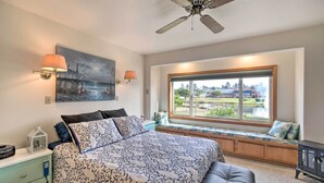 A bedroom with a large bed, a window seat, a ceiling fan, and a view of a lake and buildings. - Pet-friendly Ocean Park Home w/ Decks & View! (Ocean Park)