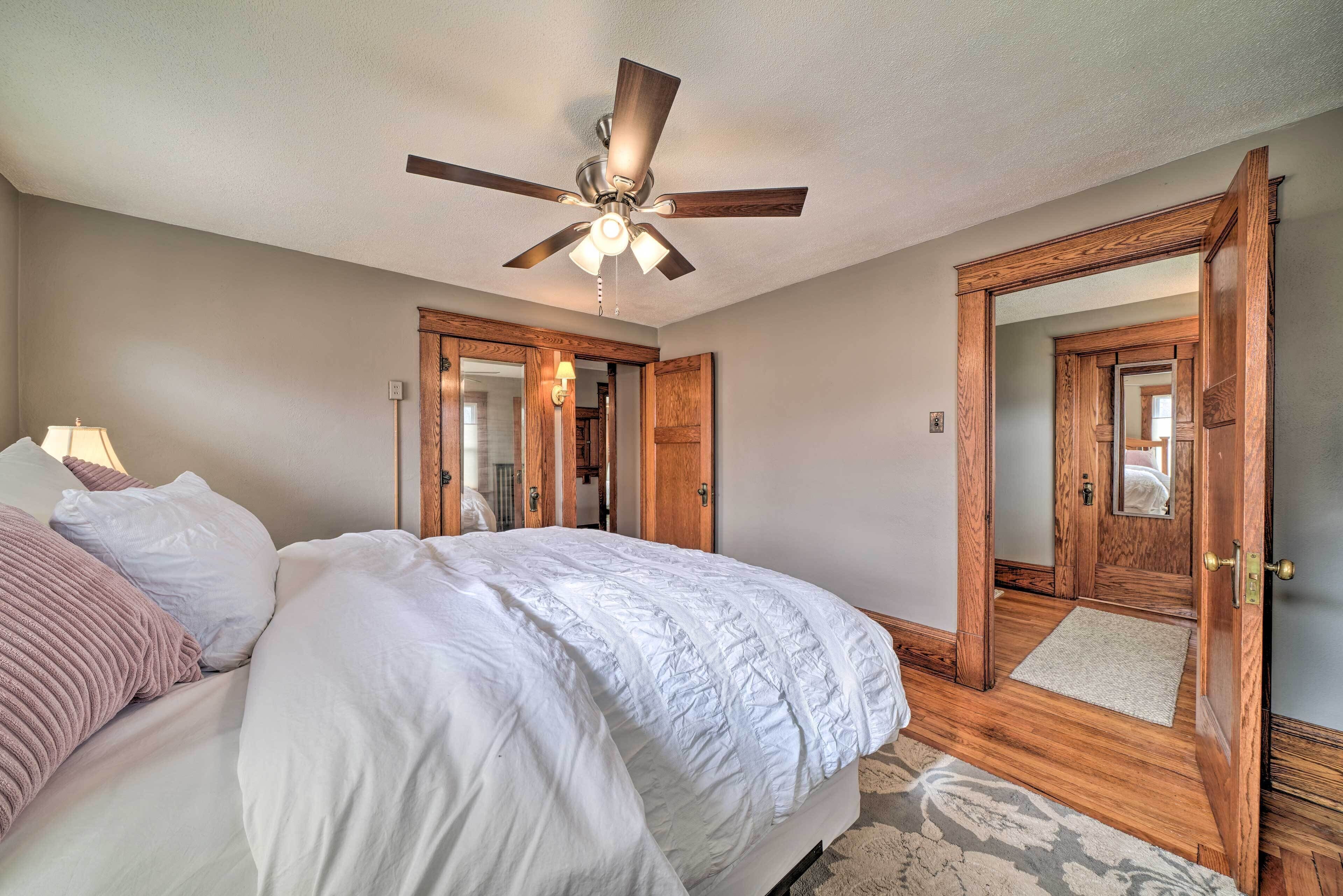 A bedroom with a bed, a ceiling fan, wooden doors, and a mirror.