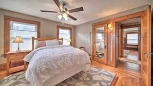 A bedroom with a large bed, wooden floors, a ceiling fan, and a view through an open door. - Classy Colonial House w/ Furnished Sunroom! (North Lima)