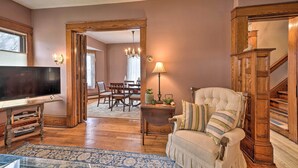 A living room with a television, a sofa, a wooden staircase, and a dining area in the background. - Classy Colonial House w/ Furnished Sunroom! (North Lima)