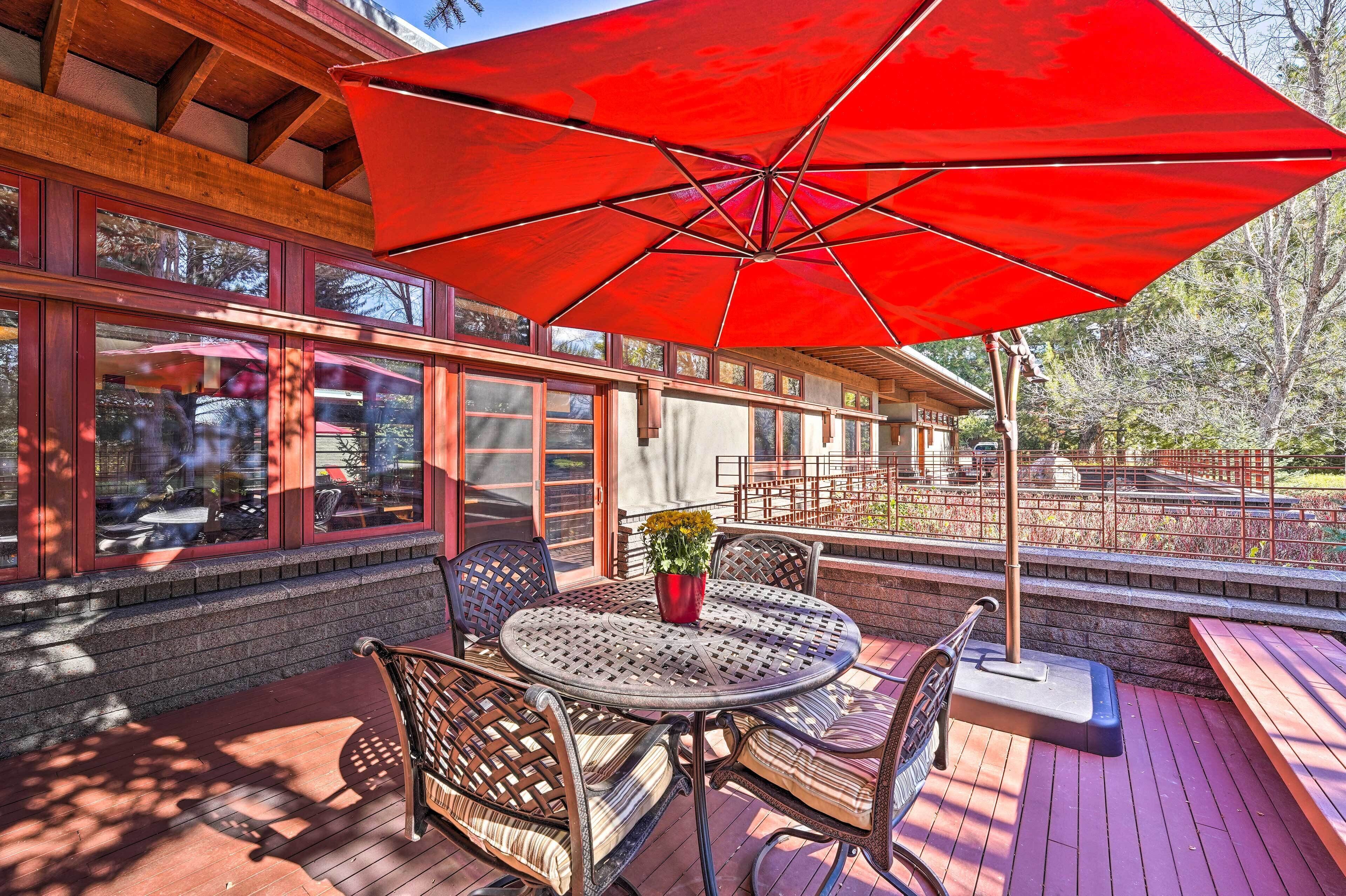 Une terrasse en bois avec une table ronde et des chaises, un parasol rouge et une plante en pot.