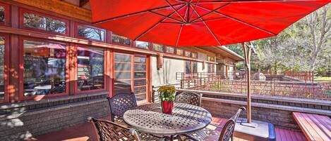 Une terrasse en bois avec une table ronde et des chaises, un parasol rouge et une plante en pot.