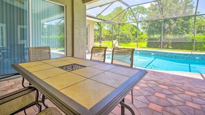 Une terrasse couverte avec une table et des chaises, une porte vitrée et une vue sur une piscine.