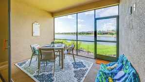 A room with a large window overlooking a body of water, a dining table with chairs, and a sofa. - Chic Country Club Condo With Pool Access! (Naples)