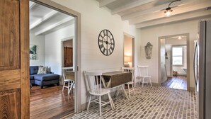 Ampla sala de estar com piso de madeira, mesa de jantar com cadeiras, um relógio de parede grande e um sofá ao fundo.