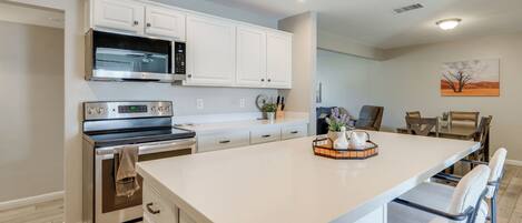 A modern kitchen with white cabinetry, stainless steel appliances, and a central island with bar stools.