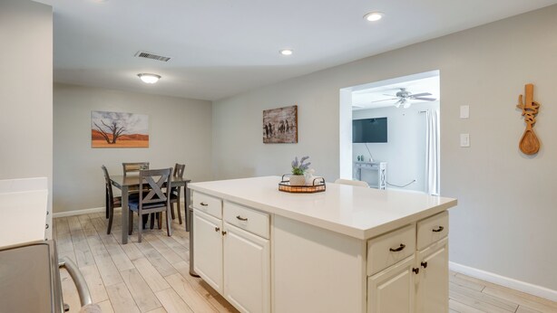 A kitchen with a central island, wooden chairs, a dining table, and artwork on the walls.