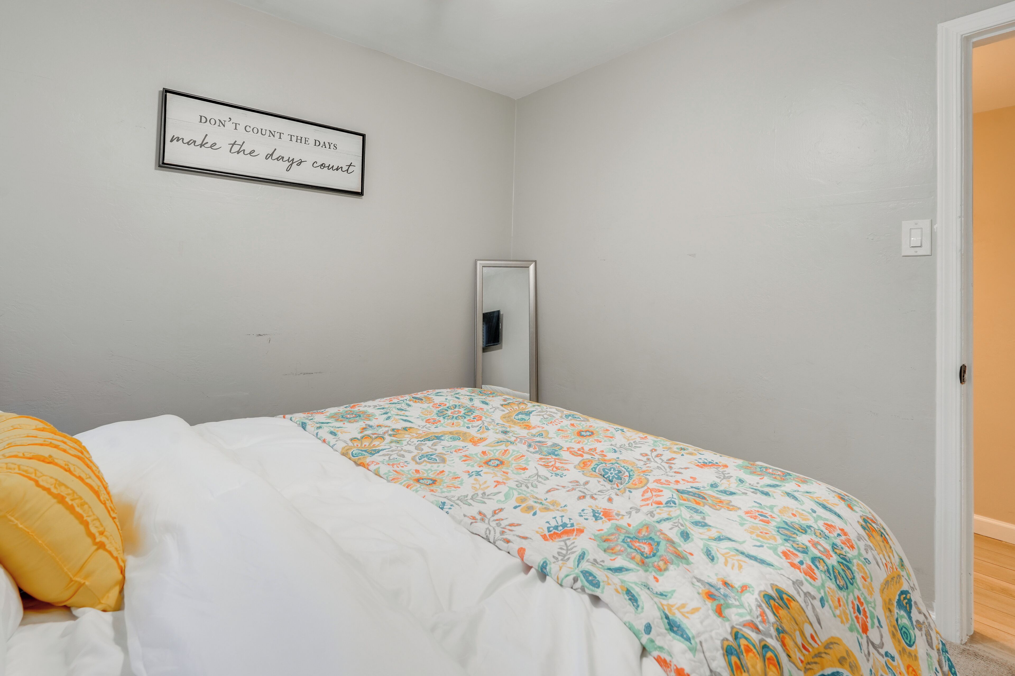 A bedroom with a bed, a wall-mounted mirror, and a motivational quote.