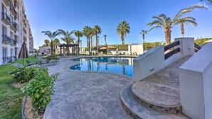 A swimming pool with a curved design, surrounded by palm trees and lounge chairs. - Walk to Beach: Modern Cabo Condo w/ Balcony! (Cabo San Lucas)