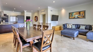 A modern living room with a dark-colored sofa, a dining table with wooden chairs, and a kitchen area in the background. - Walk to Beach: Modern Cabo Condo w/ Balcony! (Cabo San Lucas)