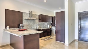 A modern kitchen with dark cabinetry, granite countertops, and a stainless steel dishwasher. - Walk to Beach: Modern Cabo Condo w/ Balcony! (Cabo San Lucas)