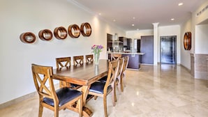 A dining area with a wooden table and chairs, a vase with flowers, and a kitchen in the background. - Walk to Beach: Modern Cabo Condo w/ Balcony! (Cabo San Lucas)