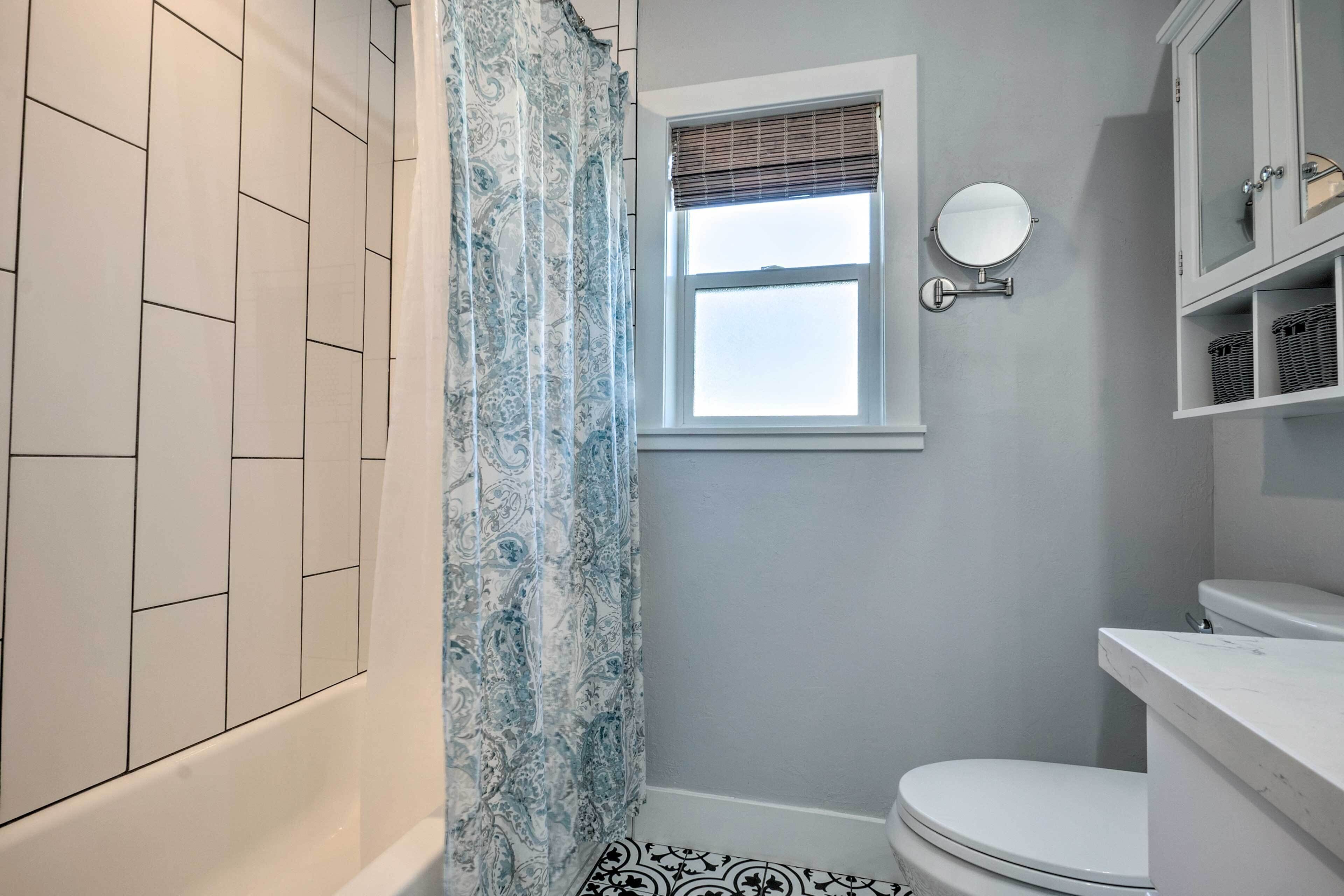 A bathroom with a white bathtub, a toilet, a window with a blind, and a mirror on the wall.